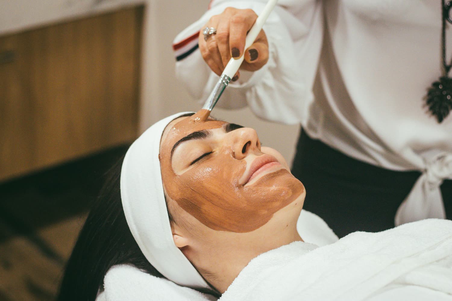 Kosmetikbehandlung mit warmer Gesichtsmaske, aufgetragen mit einem Pinsel